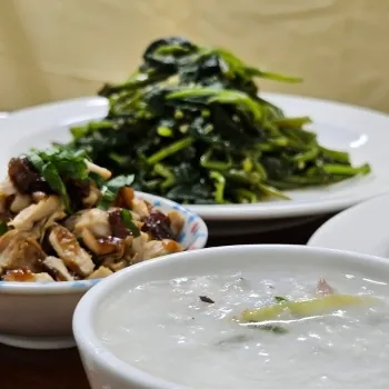 一碗米粥、一盤炒綠色蔬菜和一碗雞肉菜餚，擺放在餐桌上